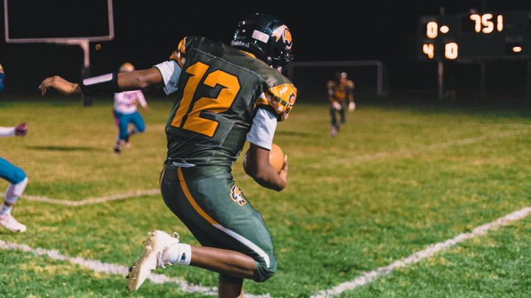 A college football player running with the ball in his hand during the game.