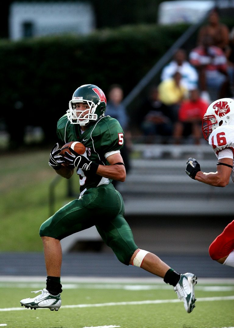 A high school receiver in a green football jersey pulling away from a defender.