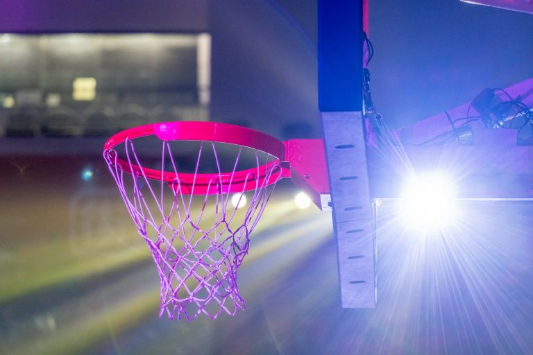 A basketball hoop dramatically lit by spotlight, used to illustrate how the NBA Round 1 spotlight tends to reveal which regular-season teams were carrying real depth and which were carrying mirages.