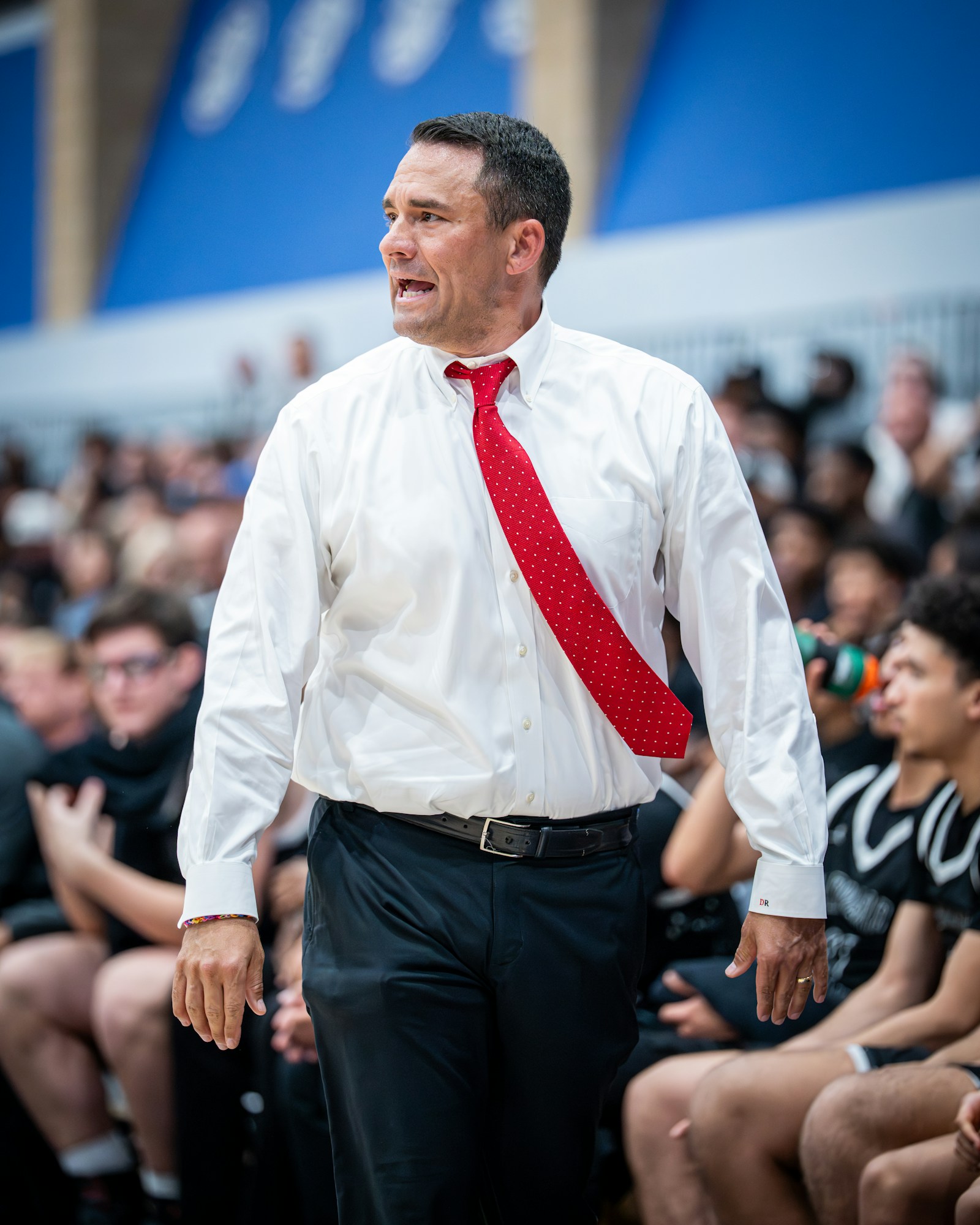 A basketball coach with red tie shouting instructions to players on the bench.