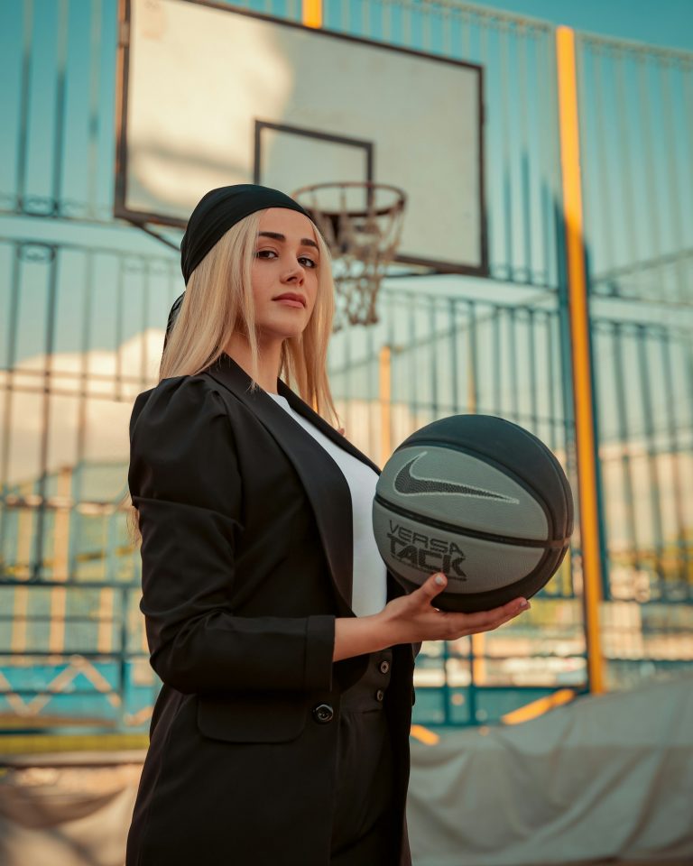 A woman holds a basketball on the court, WNBA player portrait.