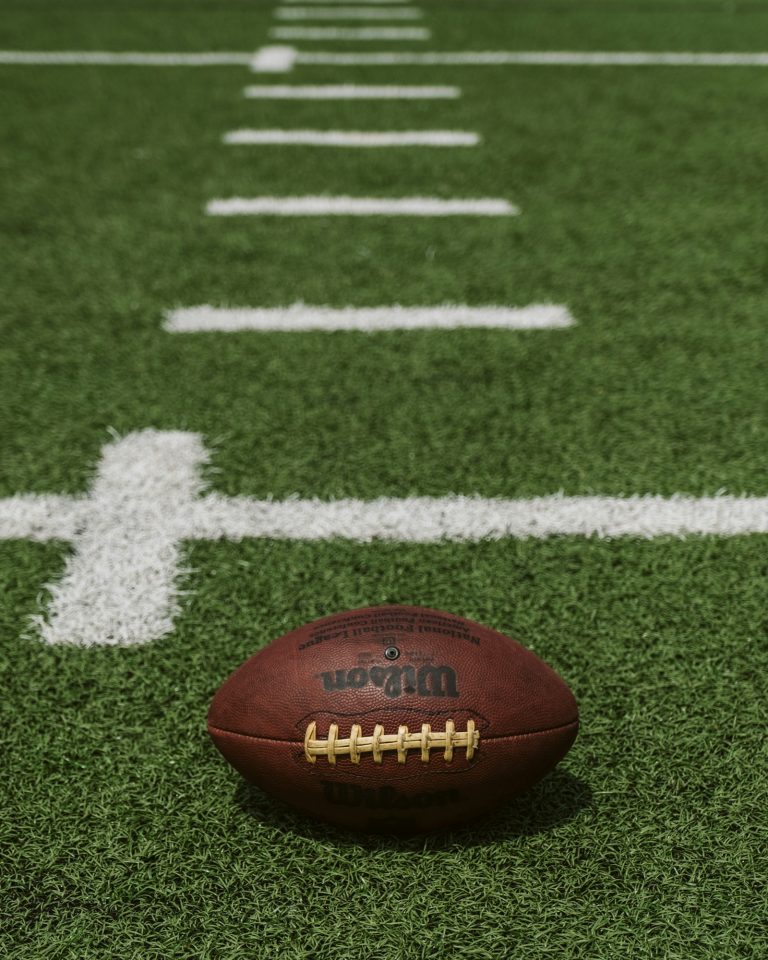 A brown Wilson football resting on a grass field, used to illustrate the red-zone evaluation dynamics that anchor modern NFL offensive analysis.