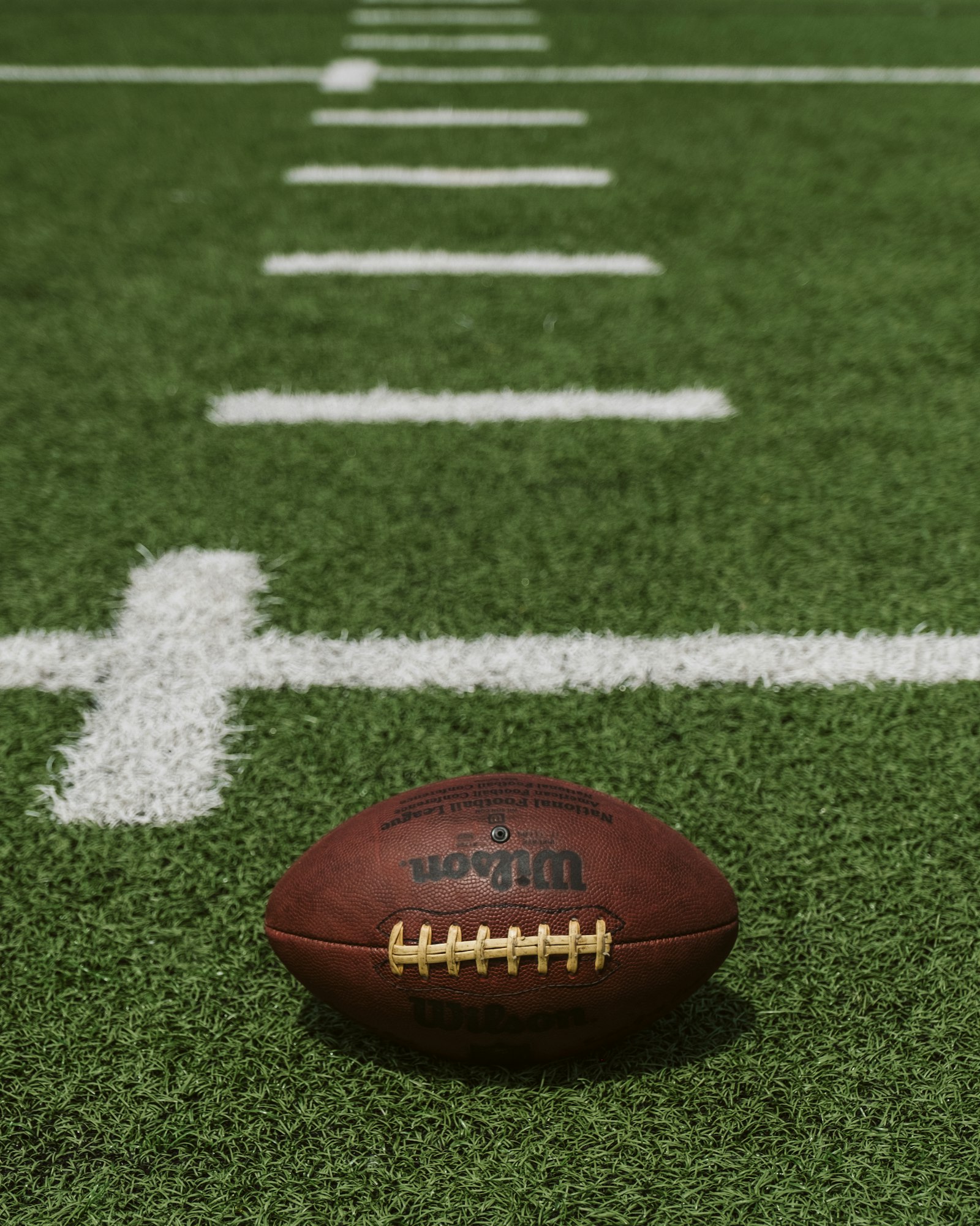 A brown Wilson football resting on a grass field, used to illustrate the red-zone evaluation dynamics that anchor modern NFL offensive analysis.