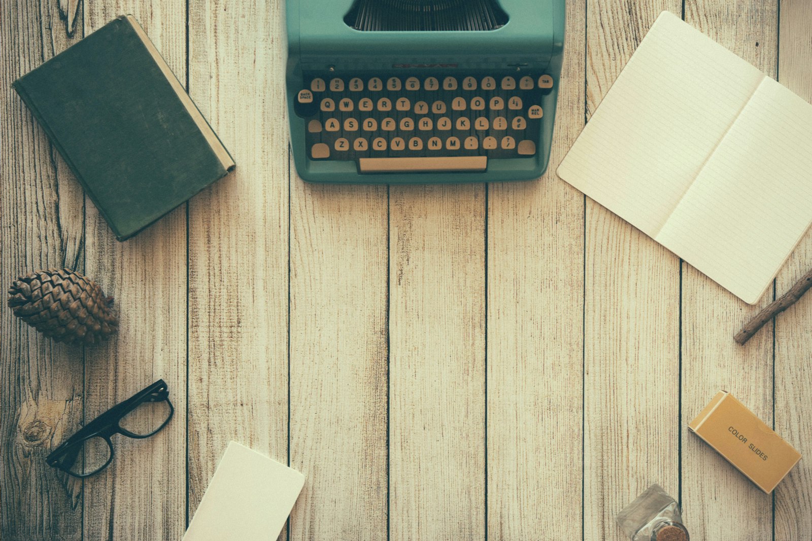 A vintage teal typewriter beside a book, used to illustrate the modern sports newsroom workflow handling Cup, Draft and Week 1 coverage.