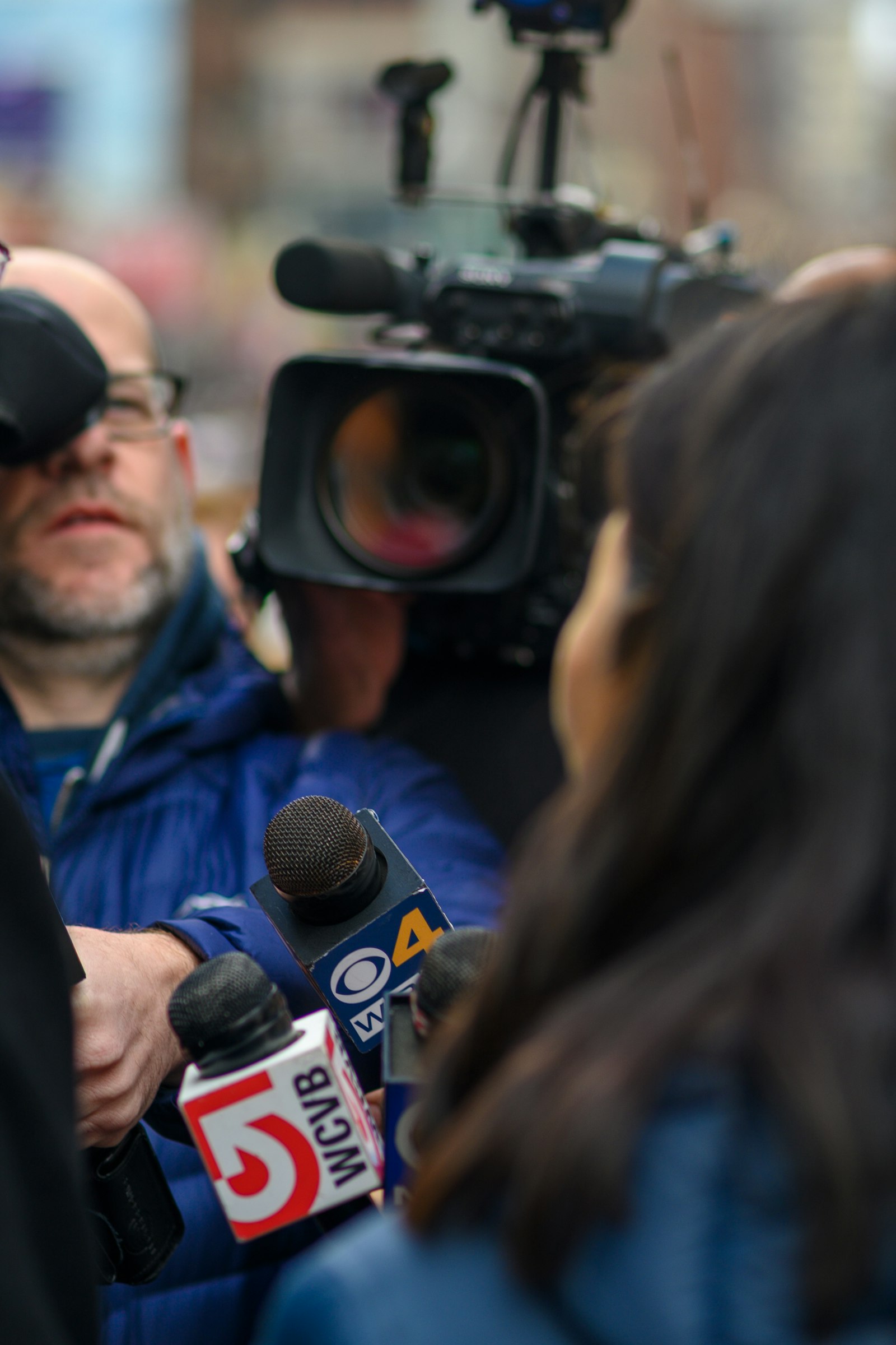 A man surrounded by reporters and microphones at a press conference, used to illustrate the modern beat-writing environment where analytics has reshaped daily coverage workflows.