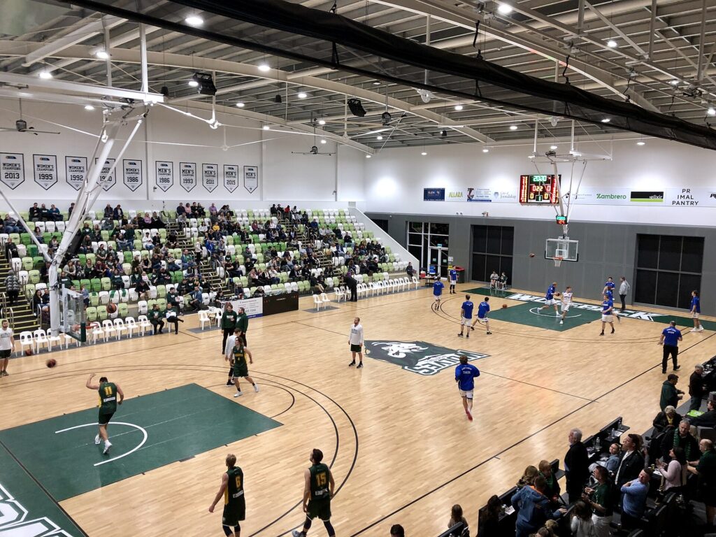 A wide view of a lit indoor court seen from high in the stands during play