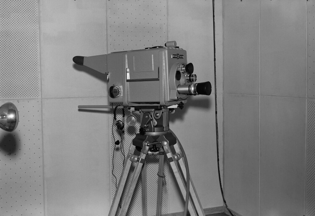 A broadcast camera on a tripod overlooking a floodlit pitch from a gantry