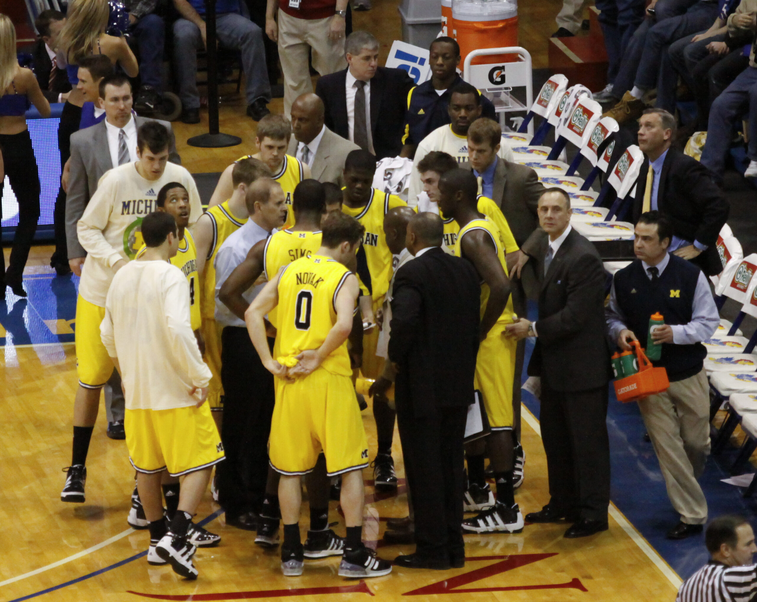 A coach crouching in front of five seated players during a break in play