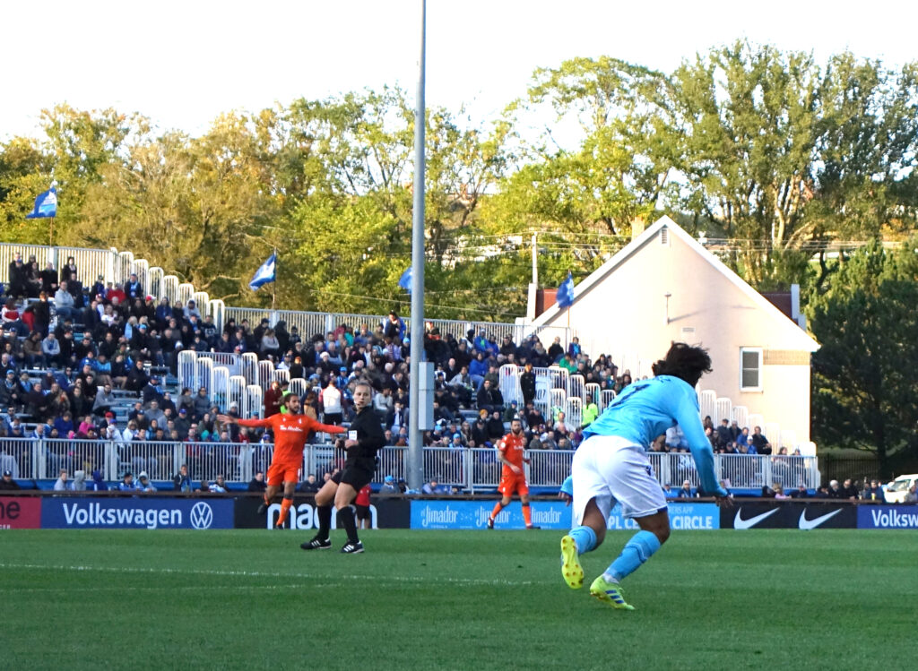An official signalling beside a group of players after a challenge near the touchline