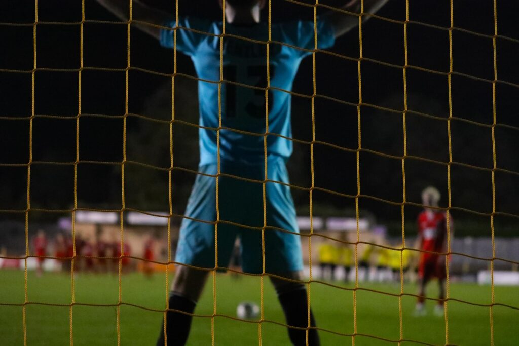 A goalkeeper set on the balls of his feet a step off his line as a shot is prepared