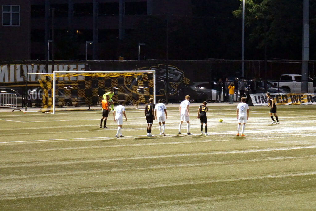 A player striking the ball inside a crowded penalty area with defenders closing in