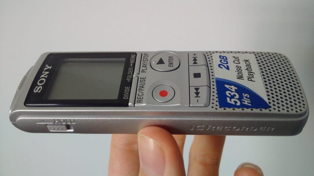 A small digital recorder held up close to catch an answer in a crowded corridor