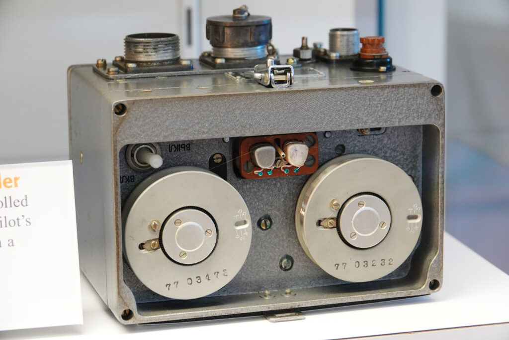 Several digital recorders lined up on a table facing a speaker's chair