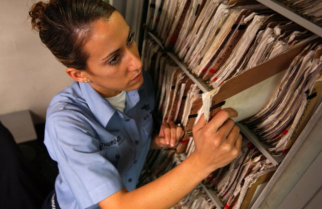 A closed folder of paper records sitting on a desk beside a pen