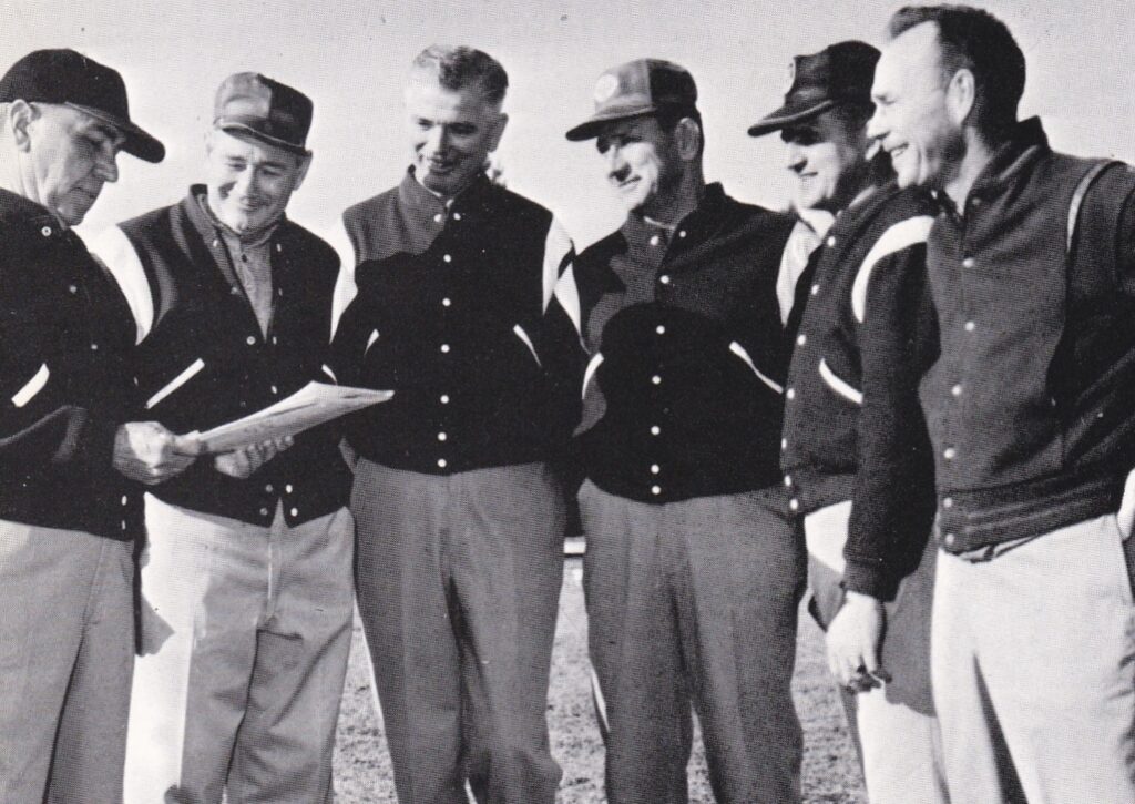 A coach standing at the edge of a marked grid holding a clipboard during a training session