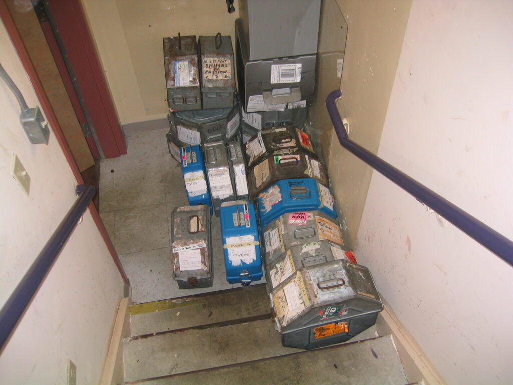 Round metal film cans labelled by hand and stacked in an archive storage area