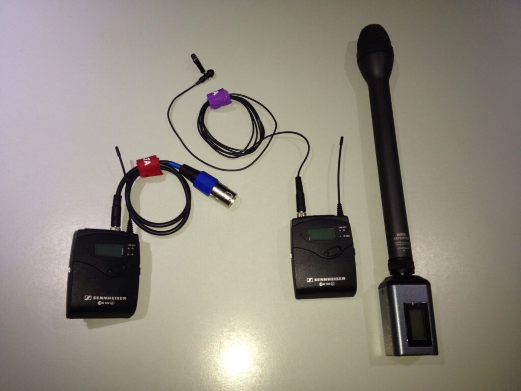 Several recorders and microphones held toward a player speaking beside a barrier