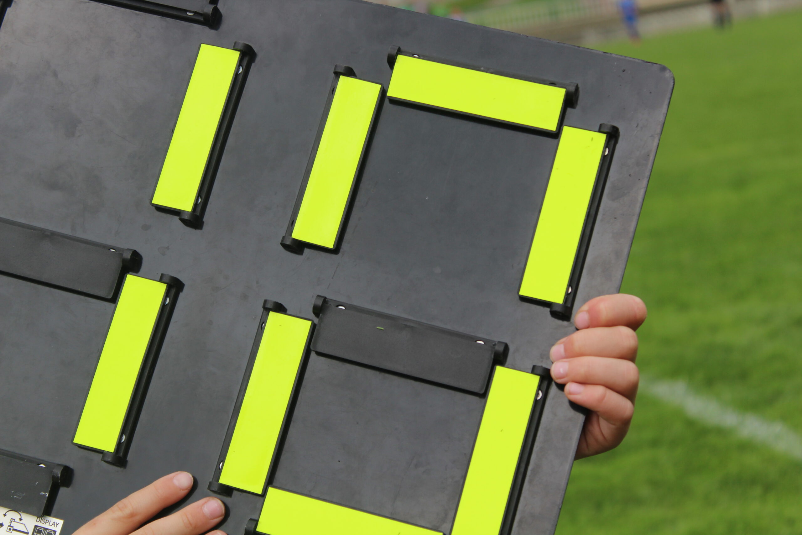 A fourth official holding up an electronic substitution board on the touchline during a match