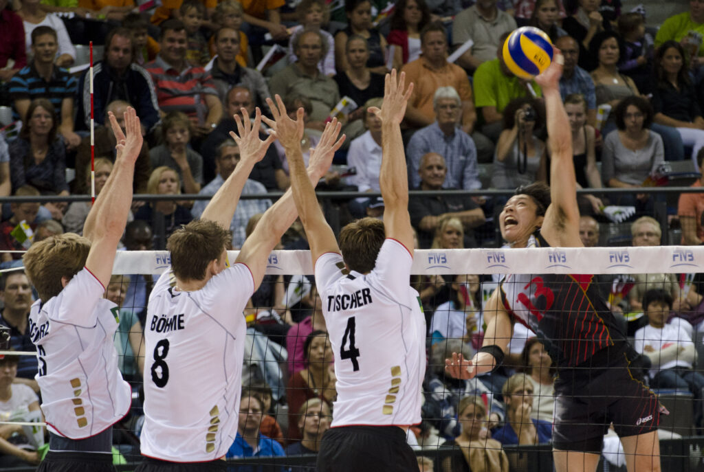 Two blockers with hands over the net trying to reach a moving attacker